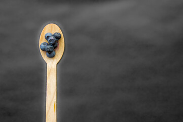 Flat lay of recycled spoon and juicy fresh blueberries on rough table. Space for text. Isolated ripe sweet bilberry fruits in eco spoon on black background. Copyspace. Healthy raw vegetarian food 
