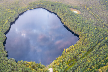 Aerial view from drone of blue deep lake with reflection of purple orange sunset clouds among autumn emerald pine, foliage forests in yellow green gold colors. Treetops in golden time in fall season