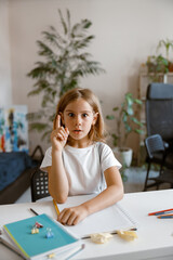 Funny little girl got idea at desk with supplies in light room