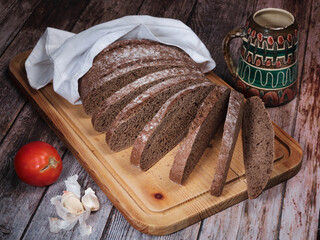 Sliced rye bread on cutting board , tomato and garlic