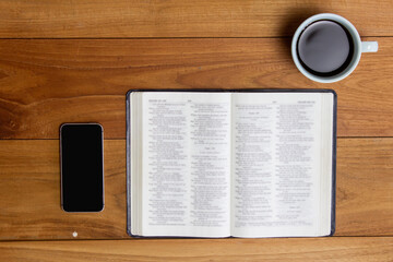 Holy Bible with phone and cup of coffee on table.