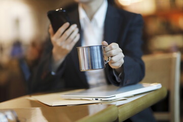 Businesswoman reading news on smartphone and drinking coffee in cafe 