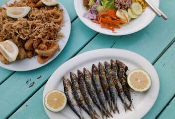 Traditional Spanish cuisine. Baked sardines, fried seafoods dish and vegetable salad on blue wooden table