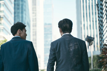 two asian business men walking on downtown street in modern city