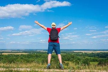 Fototapeta premium Tourist man with backpack enjoying the view in nature.Traveler man with backpack,arms outstretched stand on blue sky.