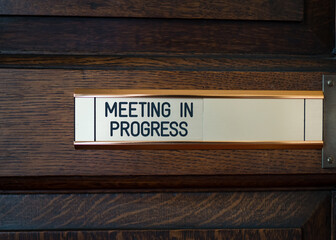 Meeting in progress metal sliding sign on solid dark oak wooden conference room door.  Do not enter...