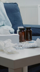 Close up of treatment against seasonal flu on table in empty room. Nobody in space with medicaments, bottles of pills and drugs, capsules, thermometer, tissues and cup of tea to cure sickness