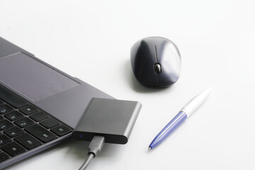 External portable SSD drive on a white background next to a laptop or ultrabook, a computer mouse and a pen. Solid State Drive. The concept of modern gadgets and connecting an SSD drive.