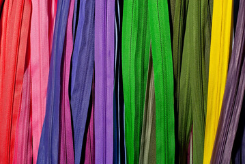 Multicolored zipper locks in a clothing store. Many colored strips of fabric hang on the wall. Clothing accessory close up.