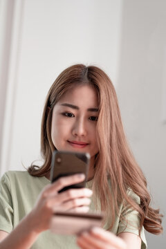 Cropped image of smiling millennial woman holding smartphone and banking credit card, involved in online mobile shopping at home, happy female shopper purchasing goods or services in internet store