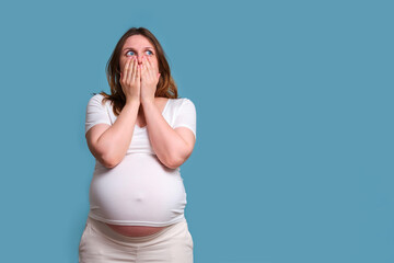 Emotion of shock in pregnant woman, studio shot on blue background - obrazy, fototapety, plakaty