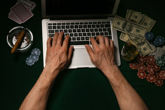 Man with laptop playing poker online at table in casino