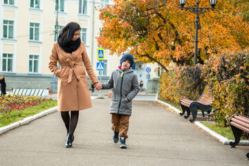 A young mother and her son are walking in the autumn city.