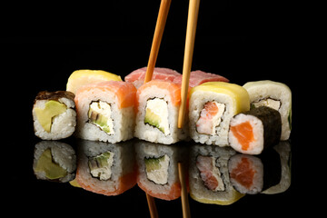 Wooden chopsticks taking delicious sushi roll on dark background