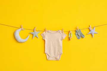 Baby bodysuit, socks and toys hanging on rope against color background