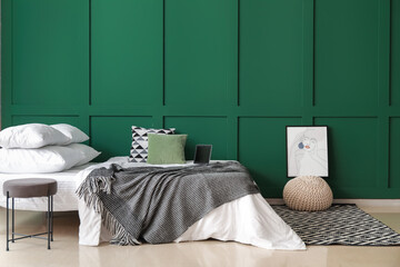 Comfortable bed with laptop, ottoman and picture near color wall
