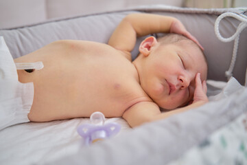 A baby boy sleeps in a cocoon on a cot. A newborn baby in a diaper is lying naked on the bed