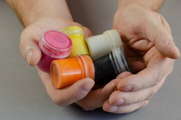 Two male palms full of gouache paints. Plastic cylindrical conta