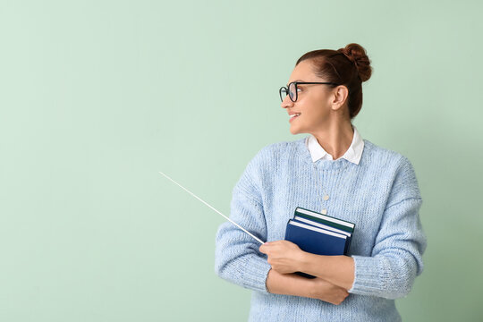 Portrait of female teacher with books and pointer on color background