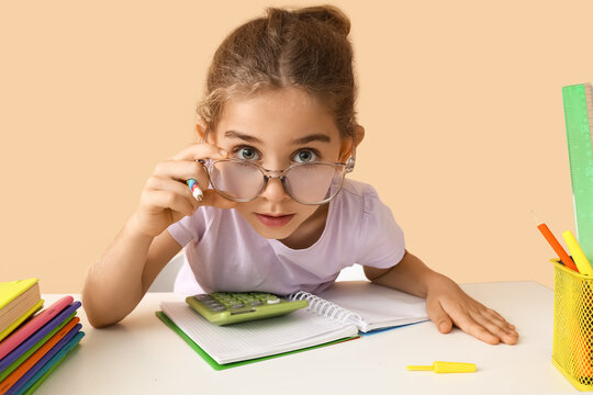 Little girl doing homework at table on color background