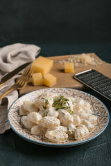 Plate of delicious gnocchi with creamy sauce on black background