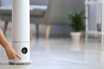 Woman switching on modern air humidifier in room