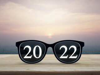 2022 white text with black eye glasses on wooden table over city tower and skyscraper at sunset, vintage style, Business vision happy new year 2022 concept