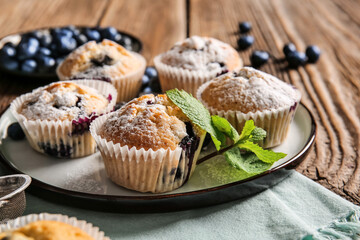 Plate with tasty blueberry muffins on wooden background