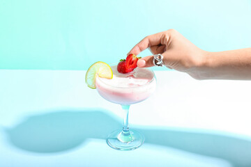 Woman decorating strawberry Pina Colada cocktail on color background