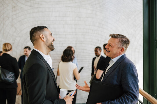 Side view of cheerful businessmen discussing during networking event at convention center