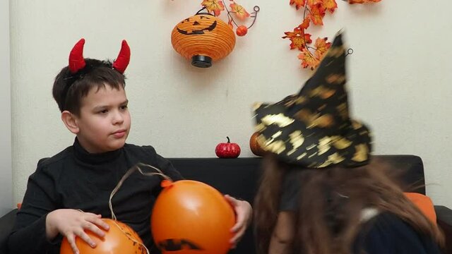 boy and girl celebrate halloween at home. eat sweets and gummy worms. girl in a witch hat and a boy with devil horns. having fun at home. family, happiness, holidays