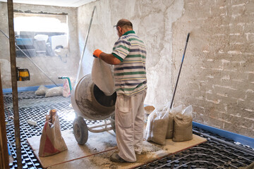 Construction worker loading a sandbag into the concrete mixer.