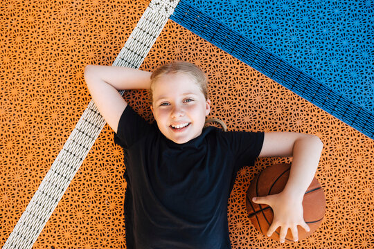 Portrait of girl with basketball lying down at sports court