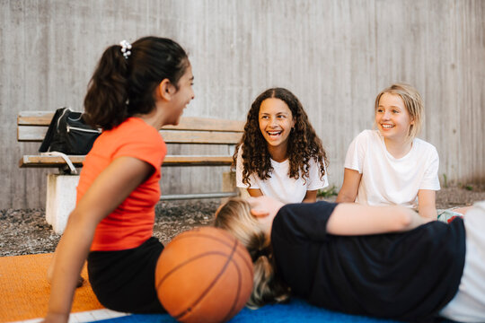 Happy female friends talking with each other at sports court