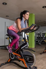 Foto op Plexiglas Full length view of a young adult woman in sportswear doing exercise in stationary bike at gym © Juan Algar