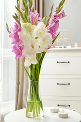 Vase with beautiful gladiolus flowers on table in room