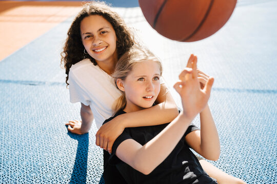 Portrait of girl sitting with female friend at sports court