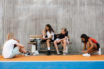 Multi-ethnic female friends talking while sitting on bench at basketball court