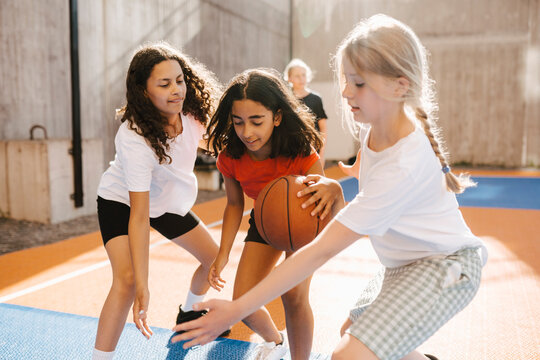 Female friends defending while playing basketball during competition at court