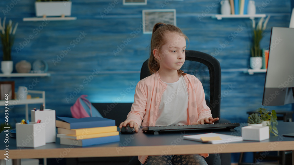 Poster little girl putting backpack on couch and using computer with keyboard at desk. young child looking 