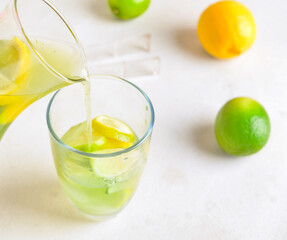 Pouring tasty lemonade from jug in glass on light background