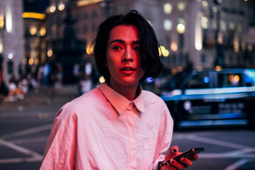 Handsome young man with long black hair holding mobile phone in city at night