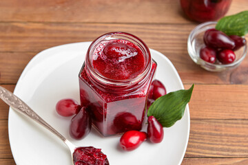 Jar of tasty dogwood jam and berries on wooden background
