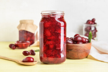 Jar of delicious dogwood jam and berries on table