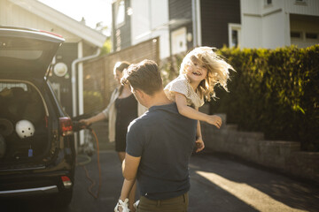 Portrait of mother, father and two daughters standing by car at electric vehicle charging station