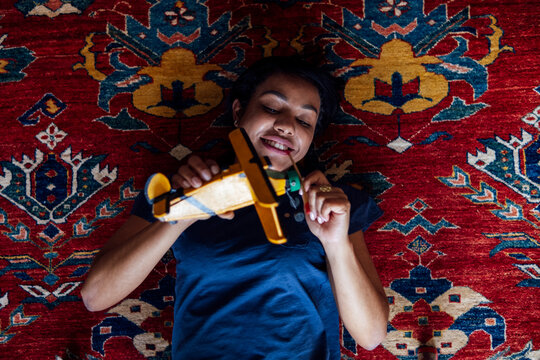 Smiling woman playing with toy helicopter while lying on carpet