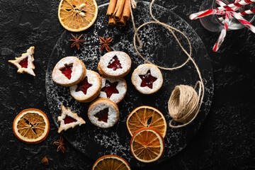 Fototapeta na wymiar Board with tasty Linzer cookies and spices on dark background