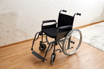 Fototapeta na wymiar An empty wheelchair in black with large wheels and manual controls on the room background. Barrier-free area. Nobody. Apartment room. House. Medical equipment rental. Copy space. Disabled mobility