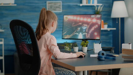 Young child playing action video games on computer at desk. Little girl losing at futuristic...