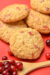 Tasty cranberry cookies and spoon with berries on red background, closeup